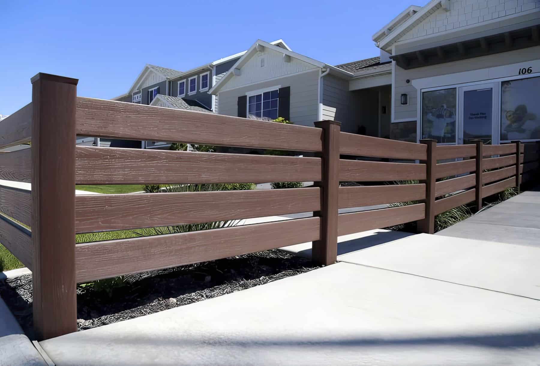 Brown vinyl fence with ranch style horizontal slats bordering front lawn with concrete sidewalk on the other side