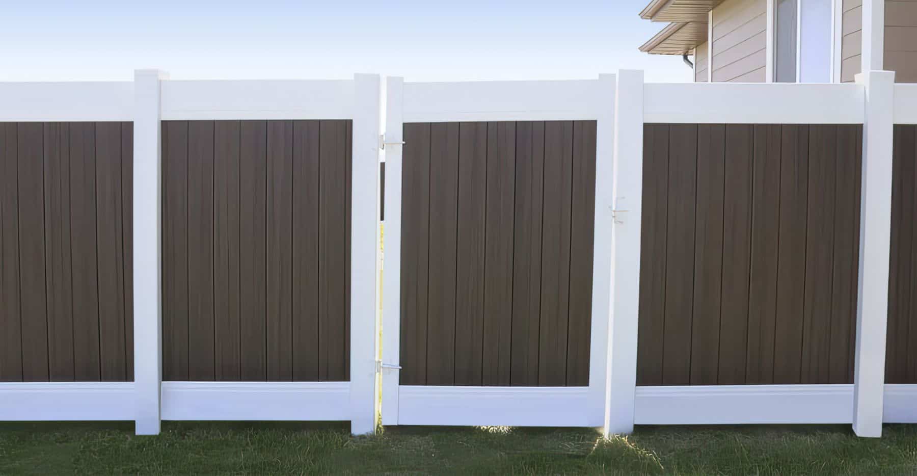 Brown vinyl fence with white borders and a gate on a grassy lawn in front of a modern suburban home.