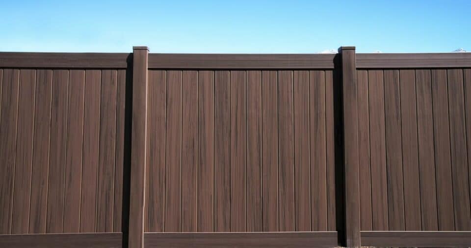 Brown vinyl fence with vertical slats and borders in front of a clear blue sky.