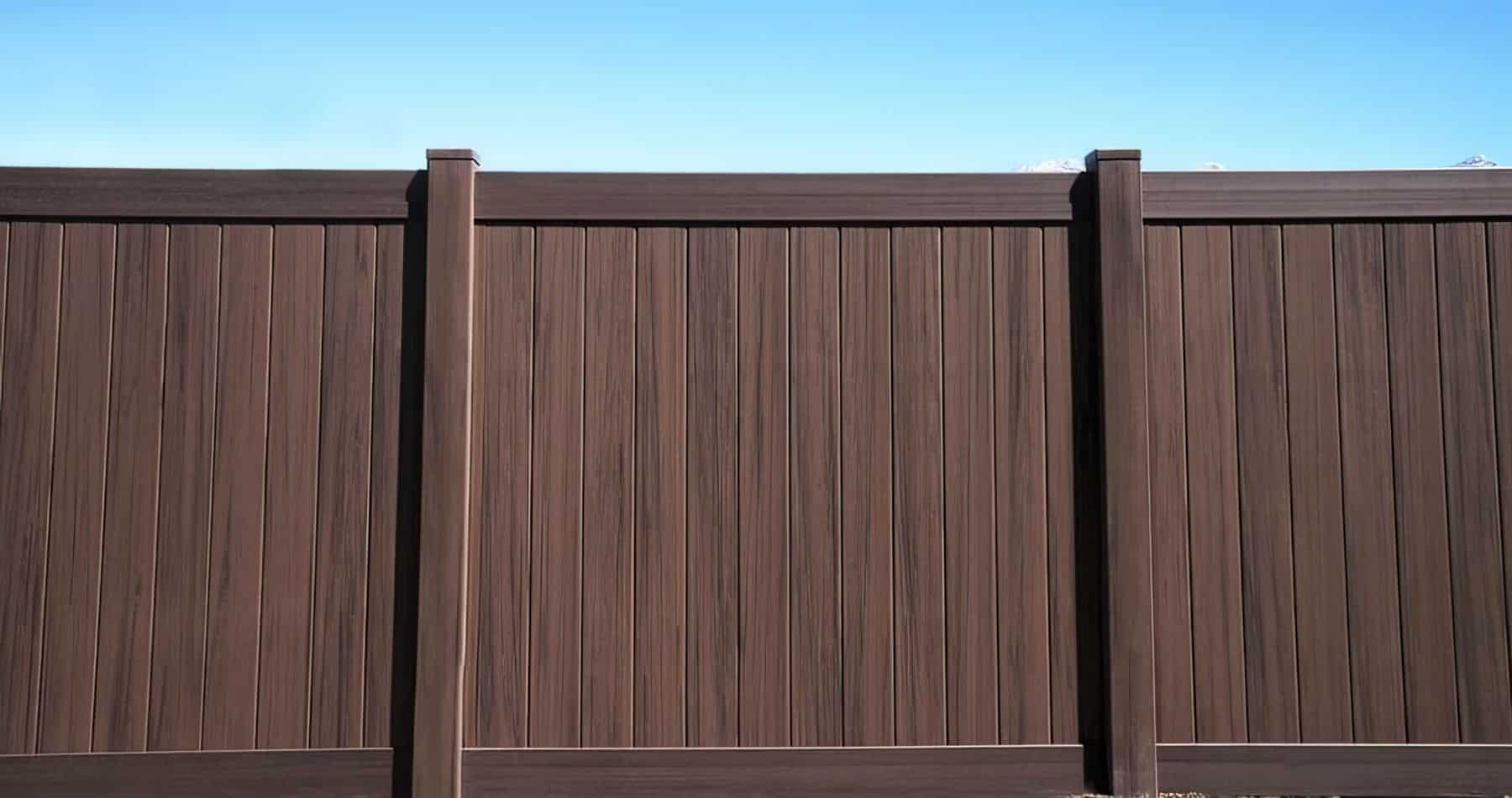 Brown vinyl fence with vertical slats and borders in front of a clear blue sky.
