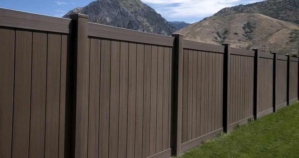 Dark sequoia vinyl fence surrounding grassy lawn with picturesque hills and a clear blue sky in the background