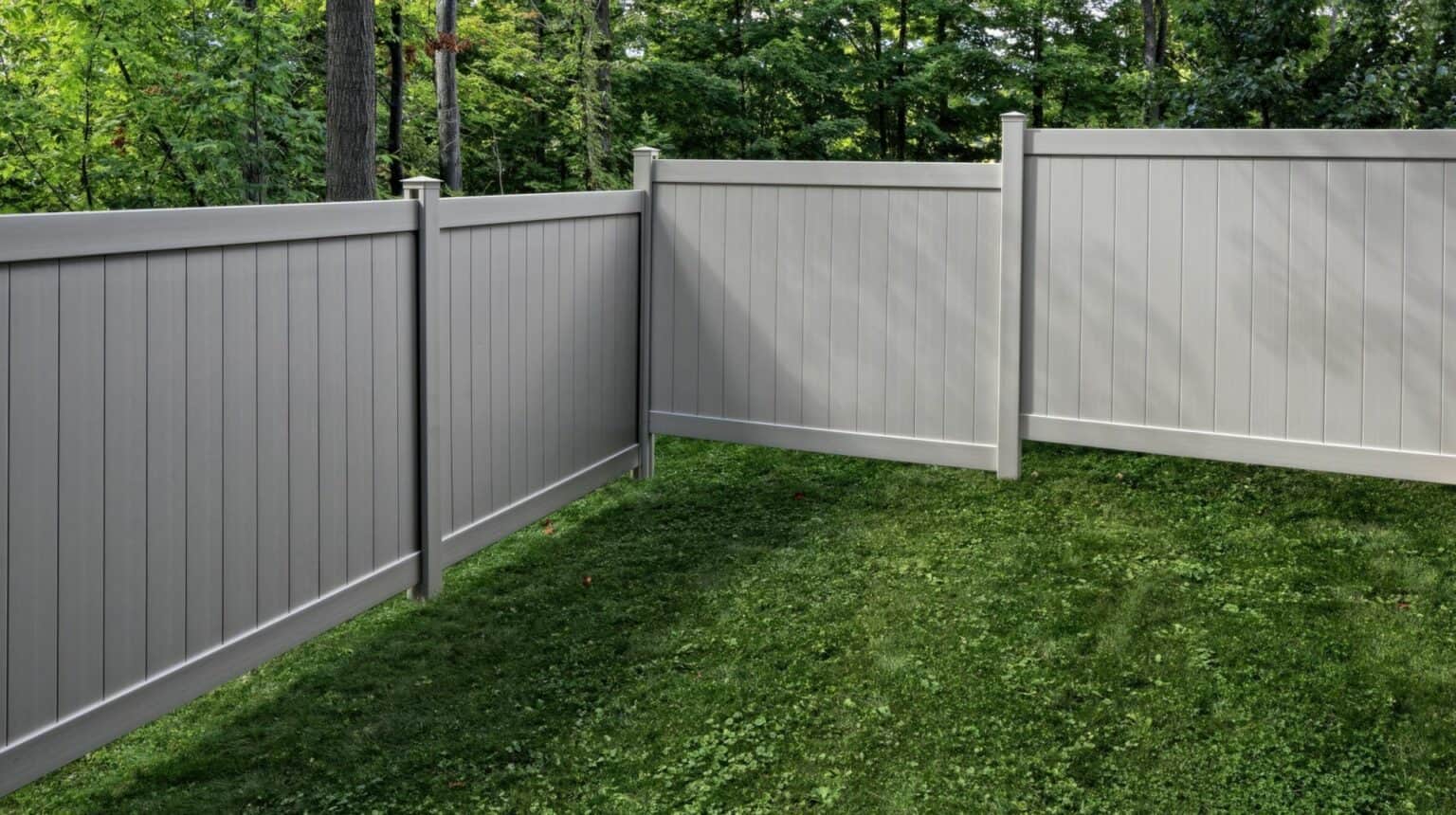 Vinyl clay colored fence in front of lush backyard lawn with dense forest in the background