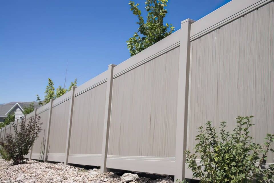 Vinyl driftwood colored fence creating boundary in front of small trees in garden on hill side.