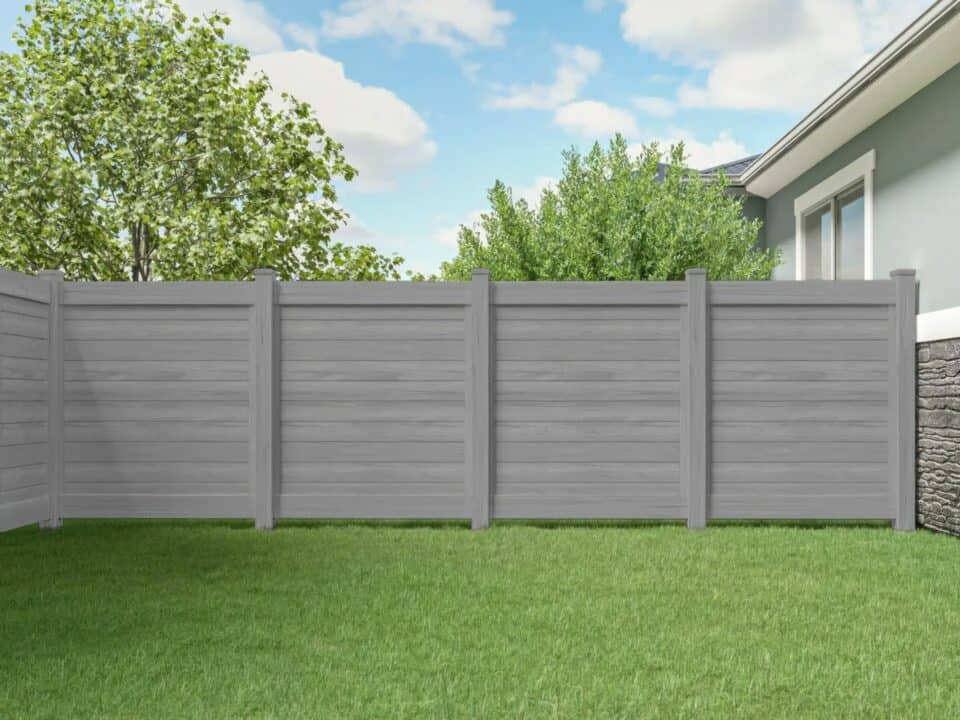 Vinyl driftwood colored fence by granite wall, grassy lawn & trees in background.