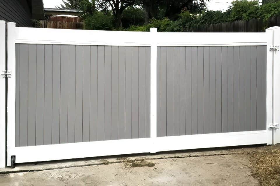 Vinyl gray colored fence with white boundary on concrete driveway leading into front lawn