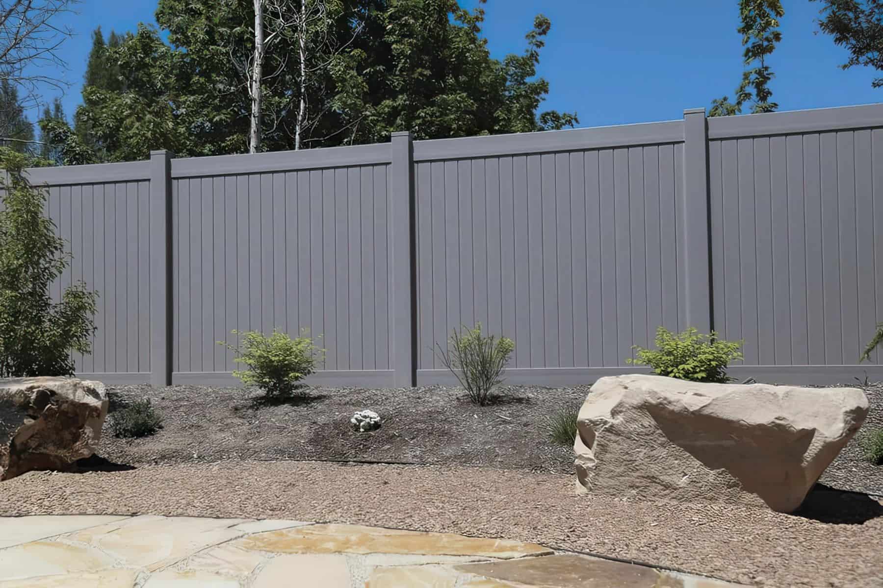 Vinyl gray colored fence, small trees & granite walkway with background trees.