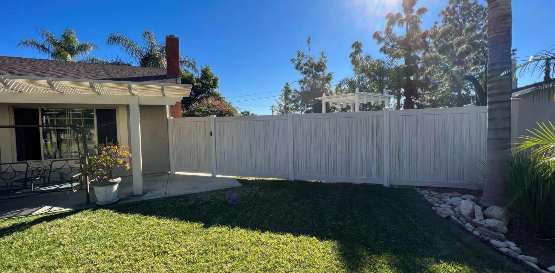Vinyl weathered aspen colored fence in backyard with lush grassy lawn, swing, and palm trees.