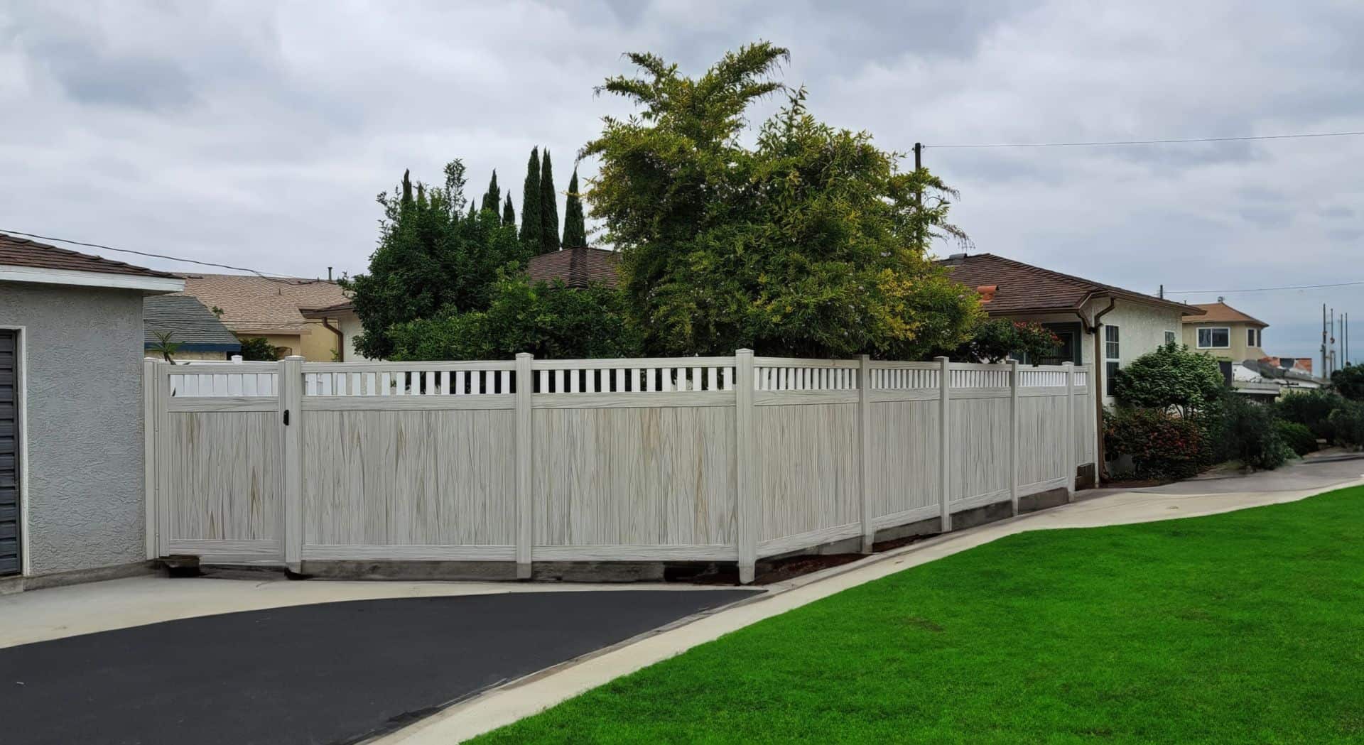 Vinyl weathered aspen colored fence, grassy lawn, trees, garage, and concrete sidewalk in serene outdoor setting.