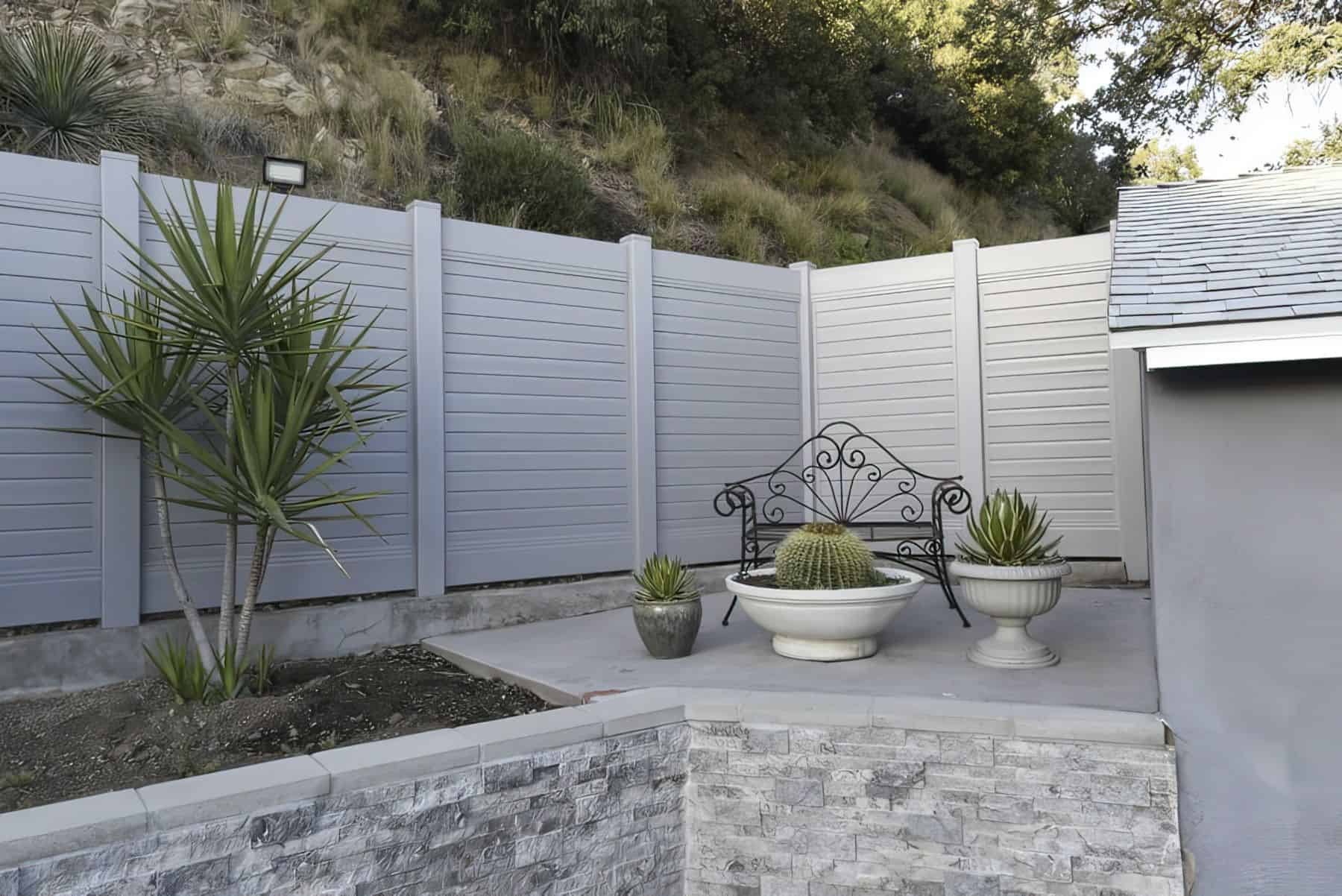 White vinyl fence creating boundary for backyard with decorative seating area and lush plants and small trees.