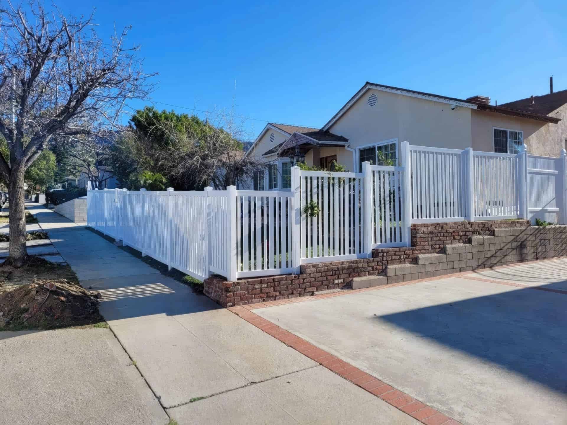 White Vinyl fence on elevated platform beside concrete sidewalk, front lawn, and distant trees create a charming suburban scene.