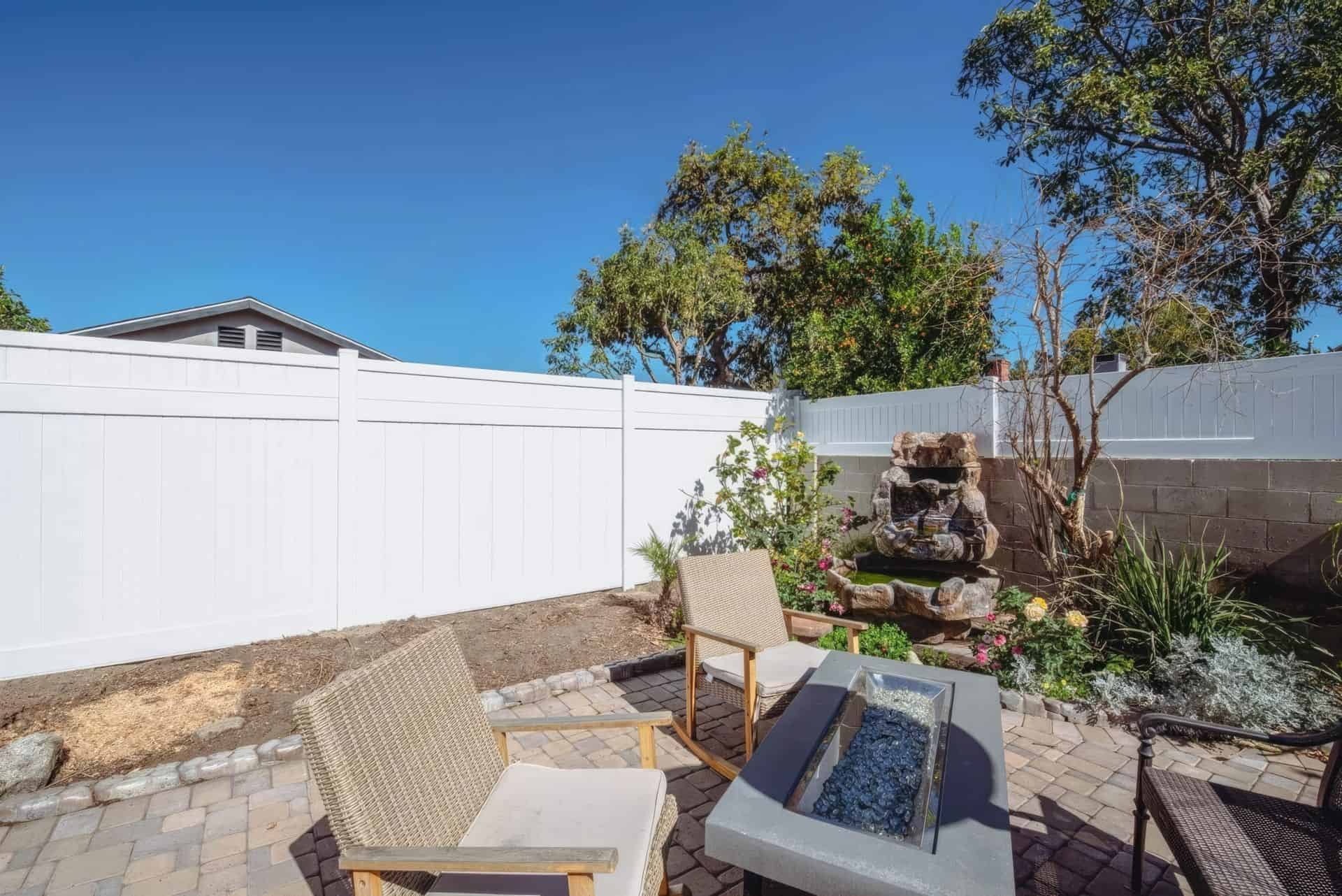 White vinyl privacy vertical fence creating boundary for backyard with decorative seating area and lush patches of grassy lawn