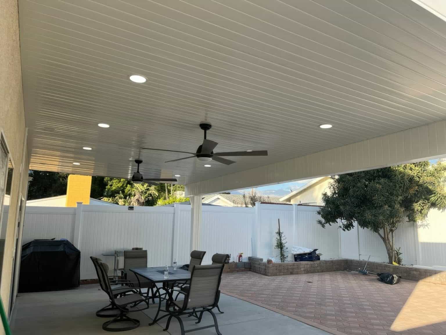 Outdoor furniture vinyl patio cover, ceiling fan, table & chairs, brick floor, and vinyl fence, creating a cozy outdoor oasis.