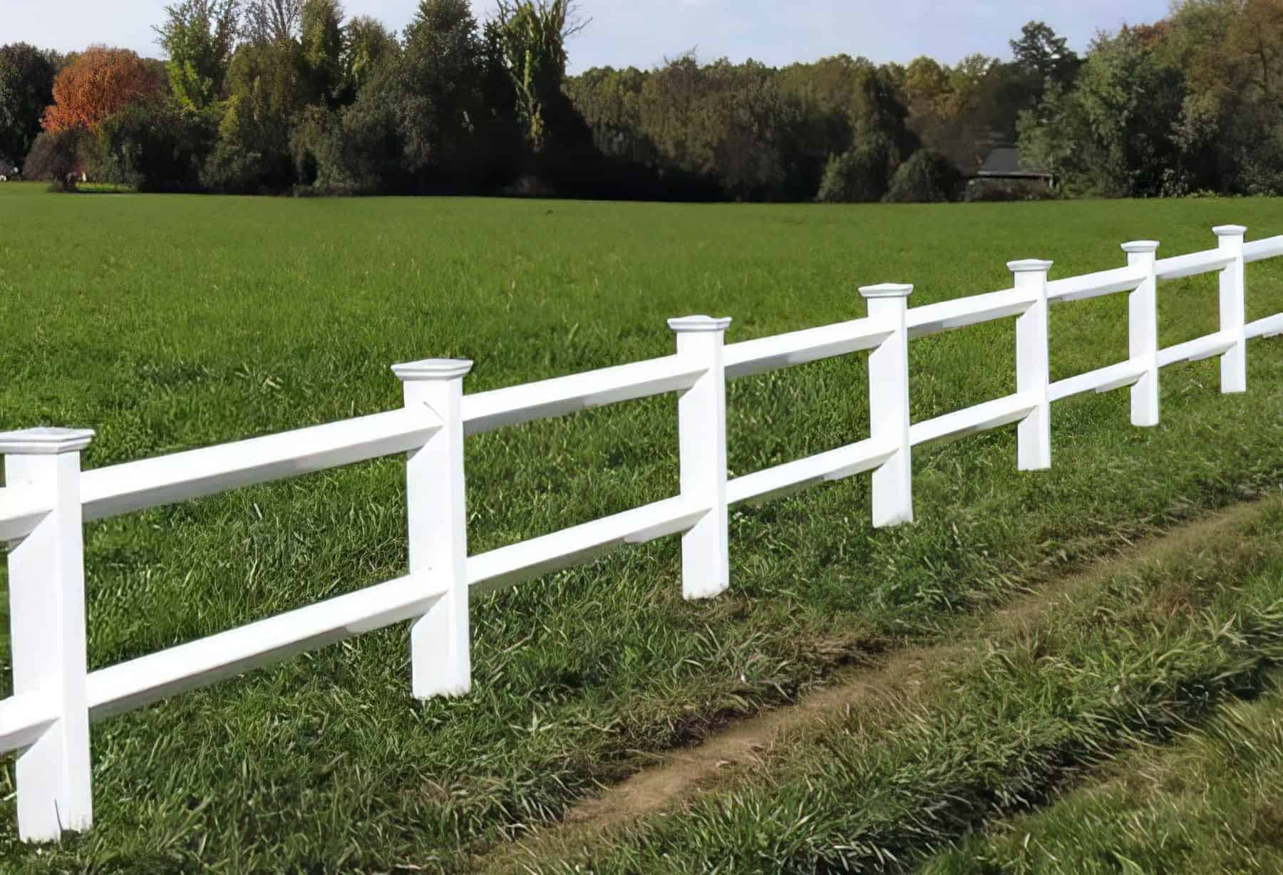 Vinyl 2-rail ranch fence in serene country setting: open field, lush grassy lawn, clear sky, trees in the background.