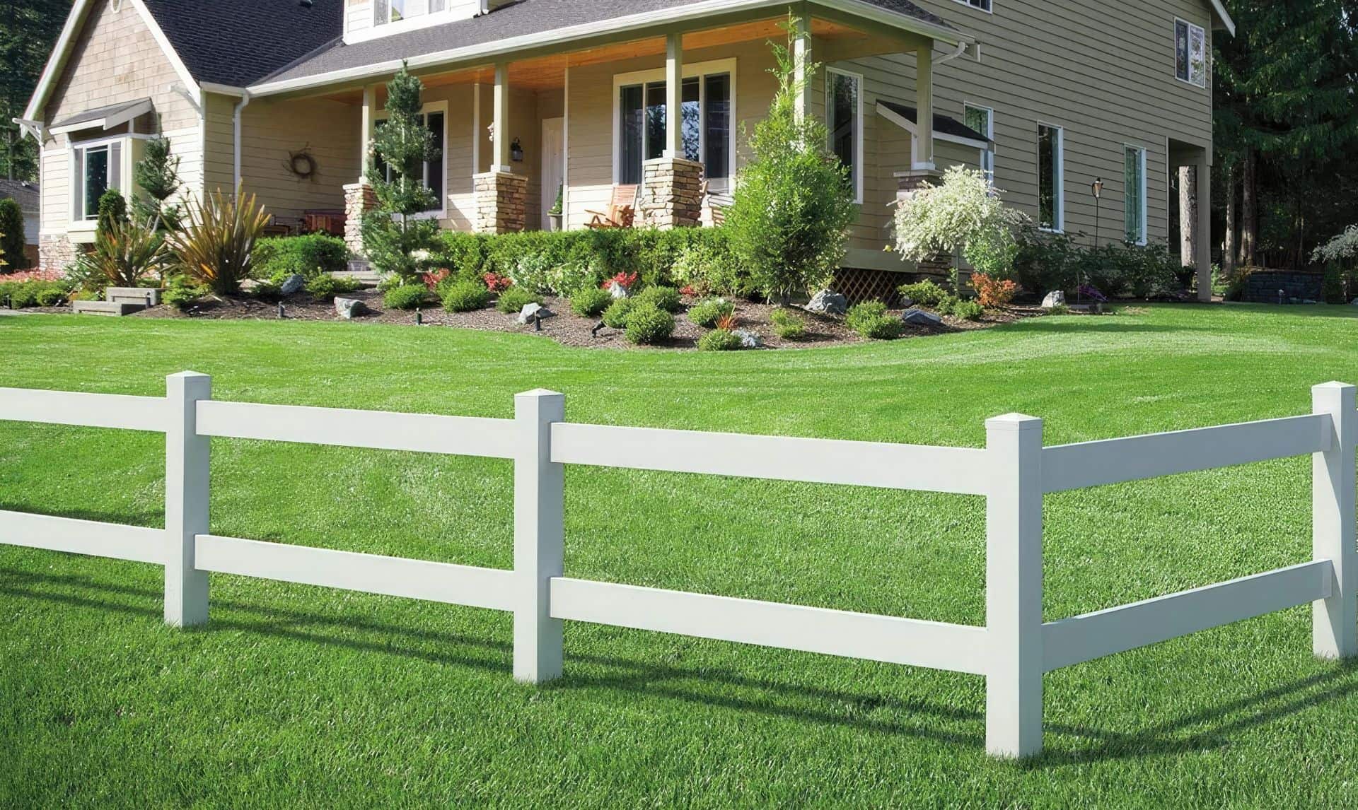 Vinyl 2-rail ranch fence surrounds suburban home in an urban setting. Grassy lawn and trees in the background