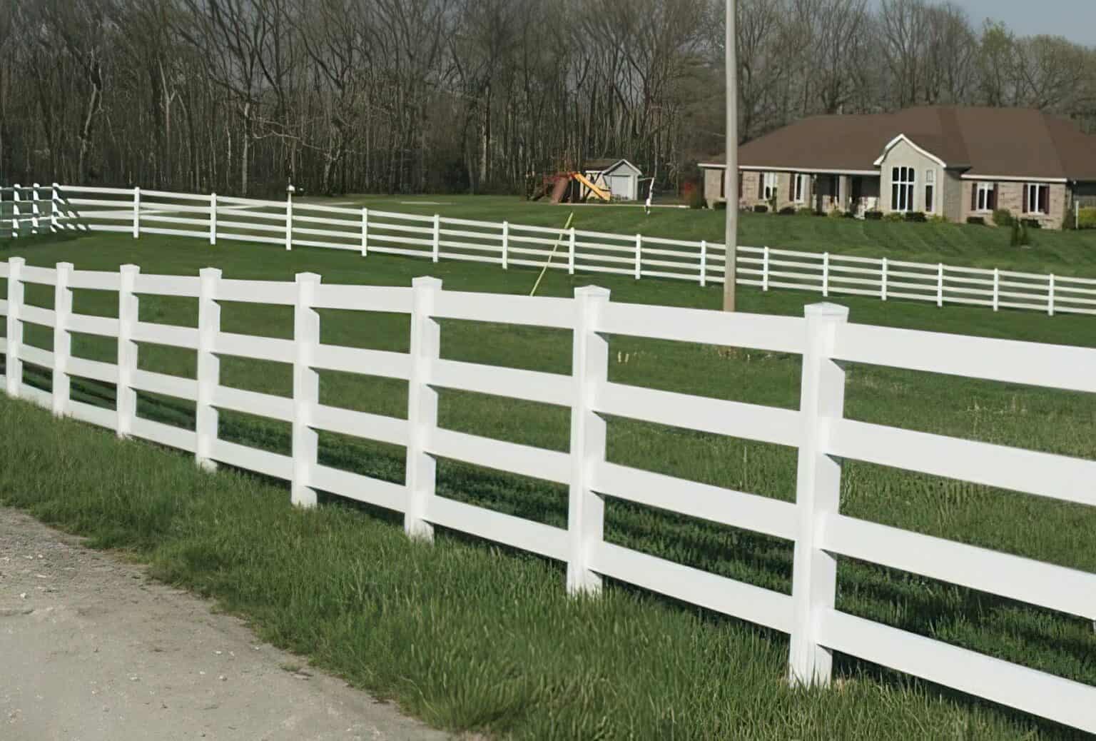 Country home with vinyl 4-rail ranch fence, concrete sidewalk, front lawn, and trees in background, set in a serene open field.