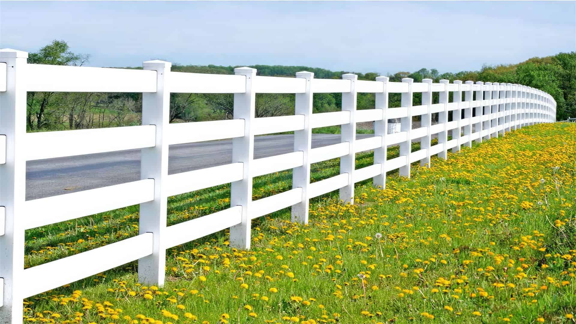 Vinyl 4-rail ranch fence amidst rural beauty: Open flower field with trees in the background. Serene countryside scene.