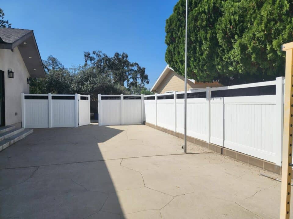 Vinyl & acrylic fence surround a concrete backyard w/ trees & houses in the background - a private & picturesque outdoor oasis.