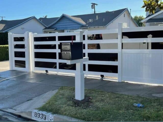 Vinyl & acrylic privacy fence, concrete floor, rolling gate, modern mailbox, trees in background - a contemporary outdoor oasis