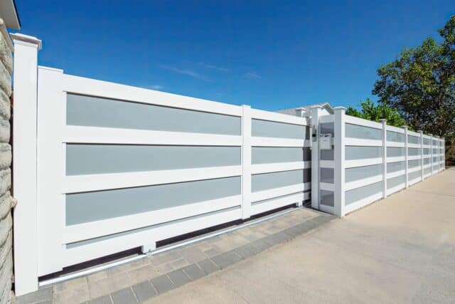 Vinyl & acrylic privacy fence, concrete floor, rolling gate, added privacy, trees in background. Stylish & secure outdoor space.