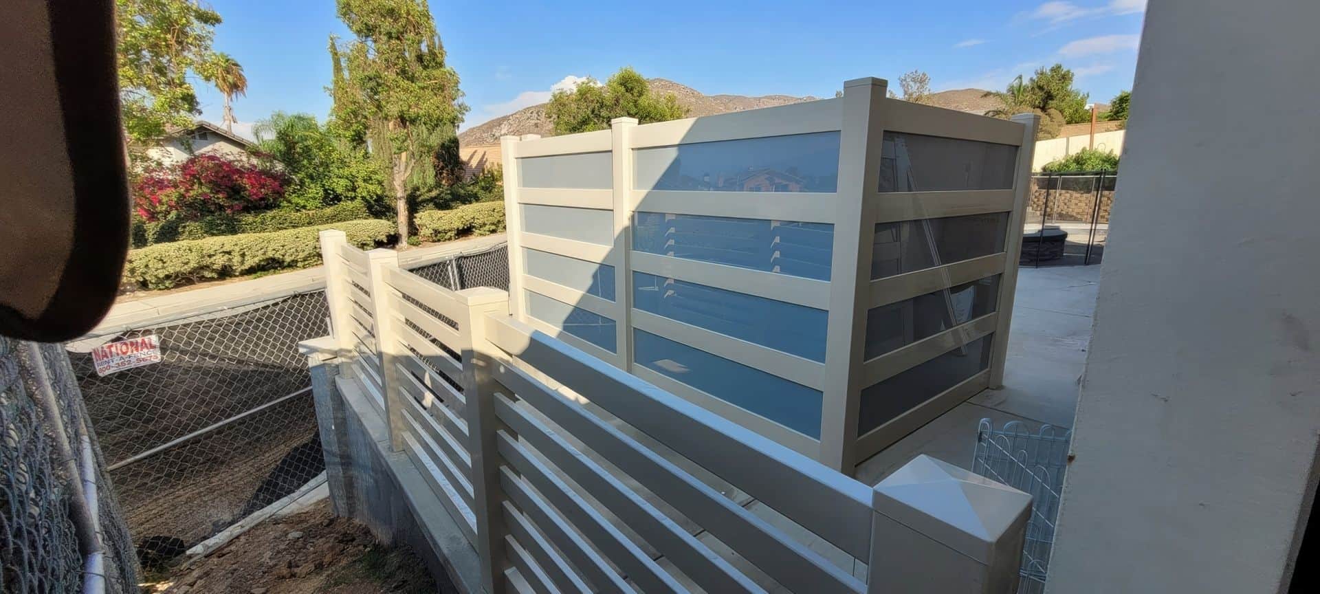 Vinyl & acrylic privacy fence, concrete floor, chainlink boundary wall, added privacy, trees in background.