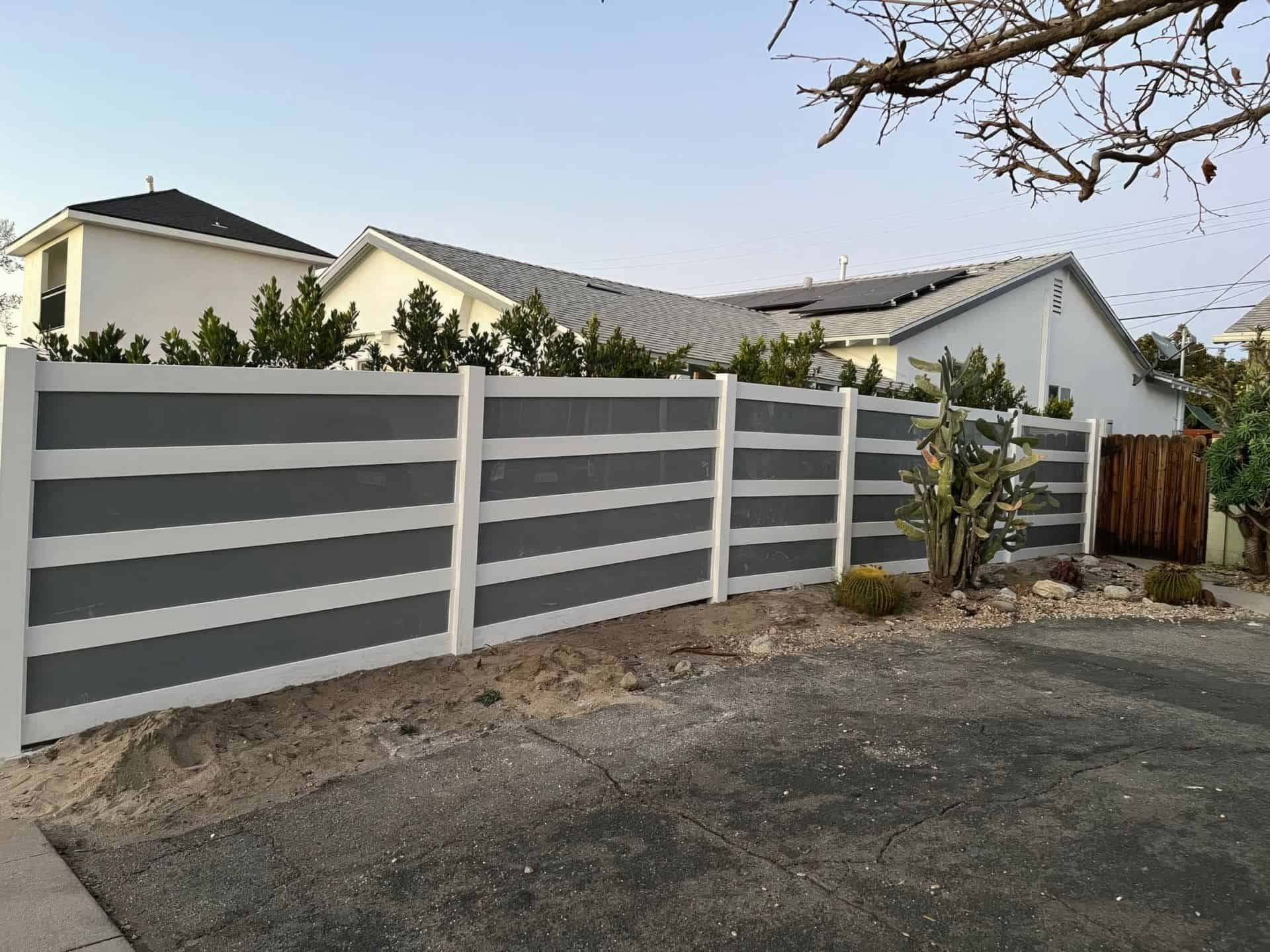Vinyl & acrylic privacy fence, concrete sidewalk, enhanced privacy with trees & houses in background.
