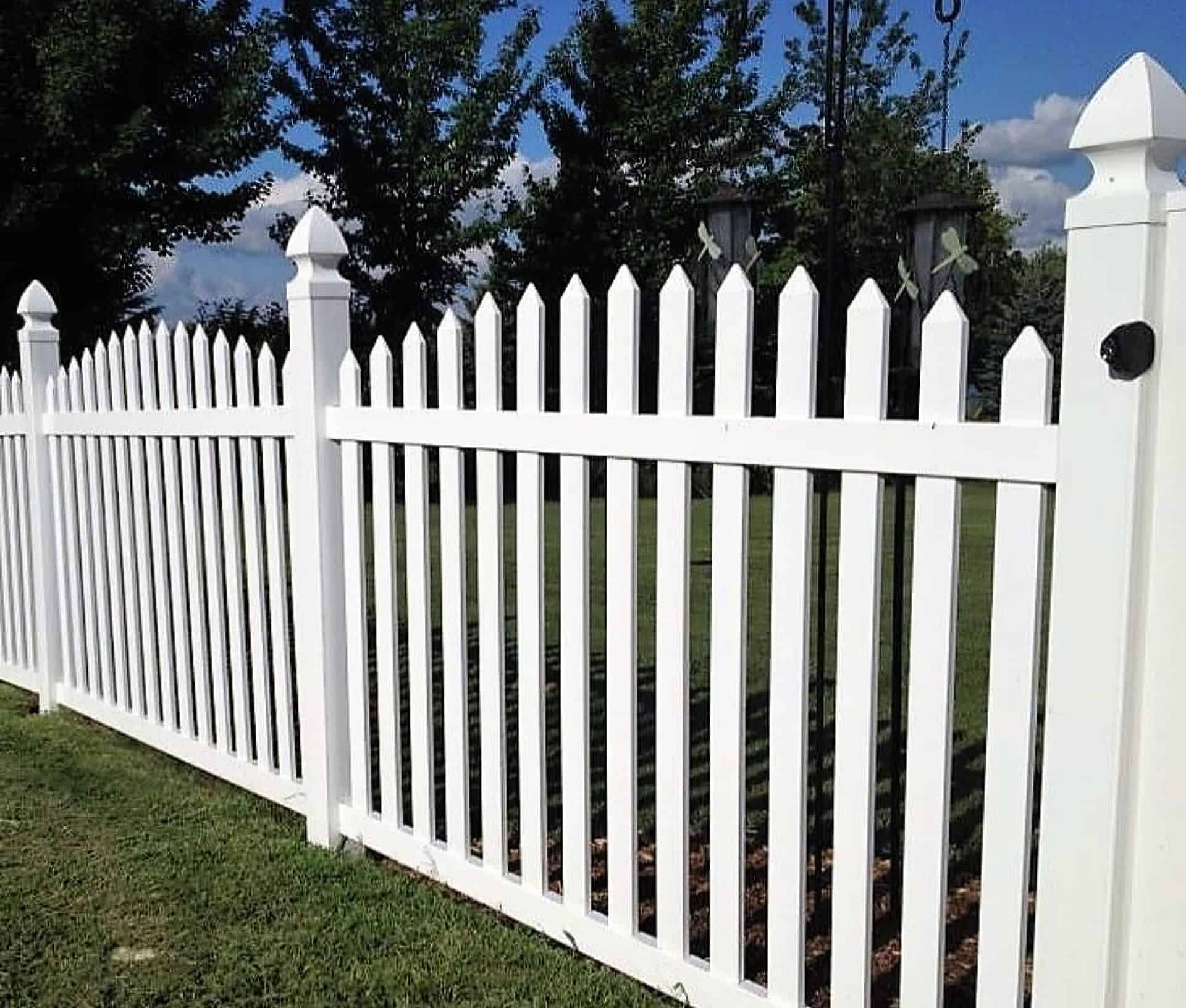 Vinyl arched picket fence with gate, on a grassy lawn with trees in the background - a charming outdoor scene