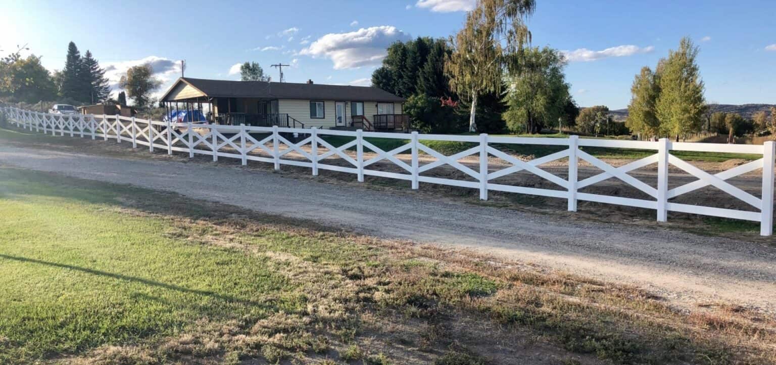 Vinyl cross rail ranch style fence surrounding farmhouse and standing adjacent to country road