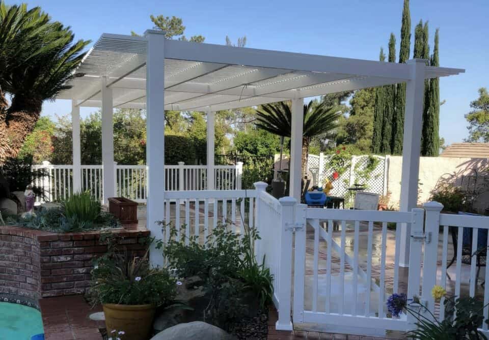 Vinyl custom patio cover & concrete floor with garden, potted plants, & distant trees creating a serene outdoor space.