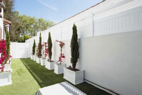 Vinyl custom wall topper enhancing concrete wall, with lush grassy lawn, potted plants, and trees in the background.