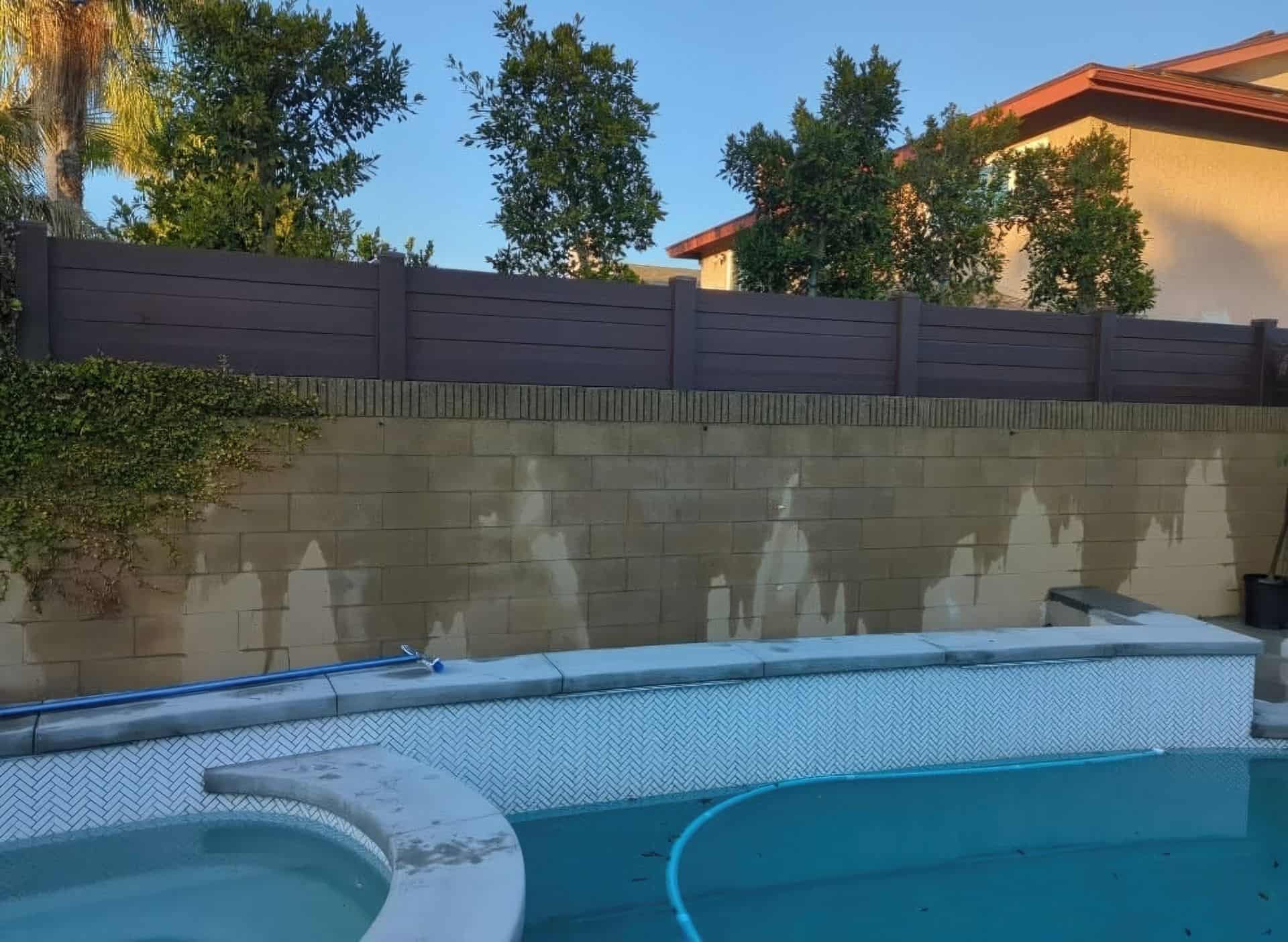 Vinyl custom wall topper adds charm to concrete wall, poolside oasis with lush trees in the background.