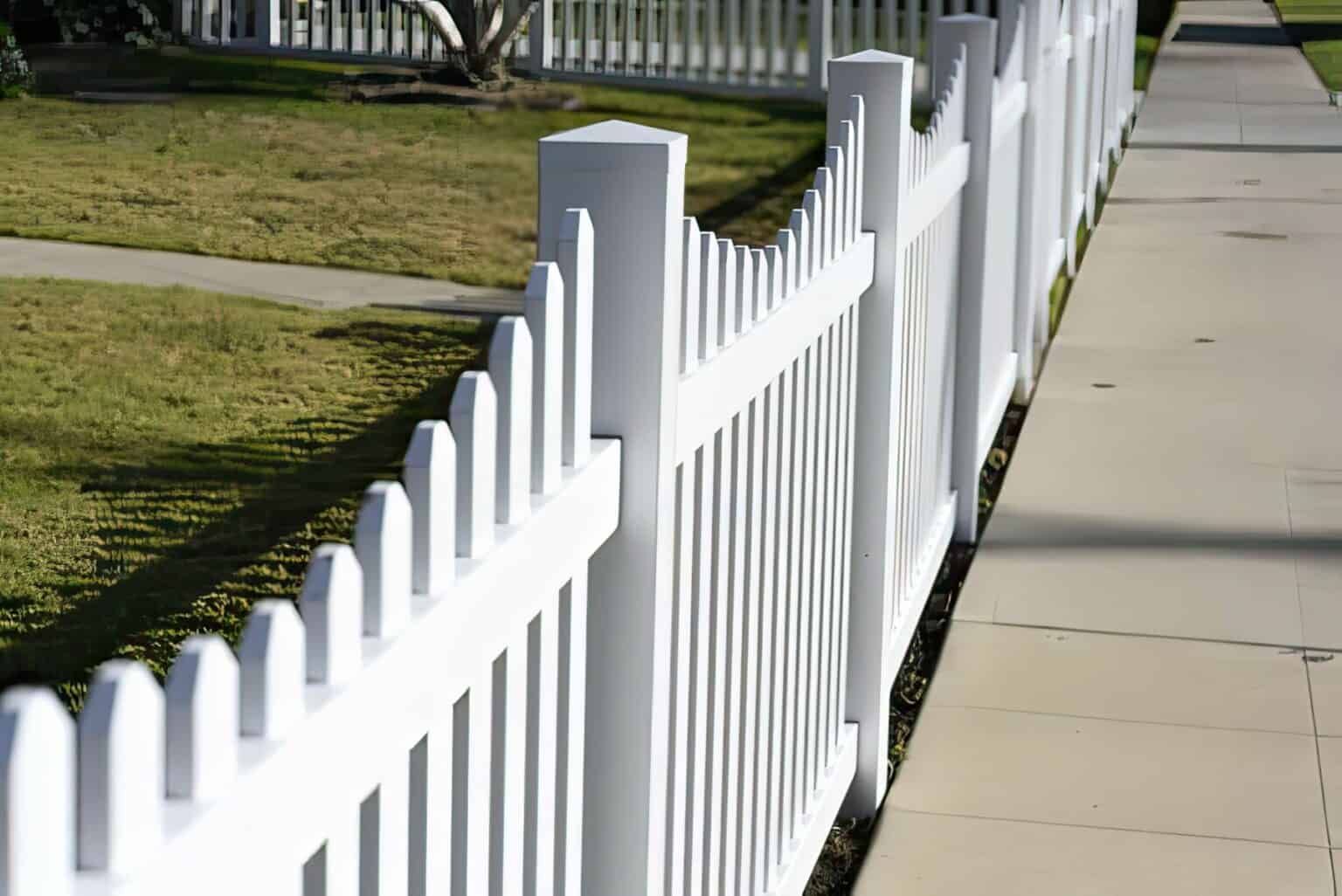 Vinyl dog ear picket fence in front of grassy front lawn with concrete walkway, with a concrete sidewalk on the other side.