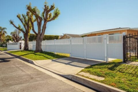 Vinyl driveway double gates block entrance to the ranch style suburban home with trees in the background