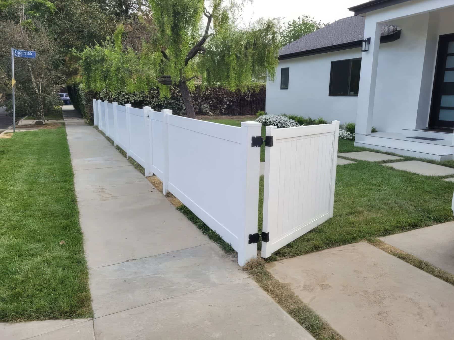Vinyl driveway double gates, suburban home, clear sky, concrete sidewalk, lush front lawn, and trees in the background.