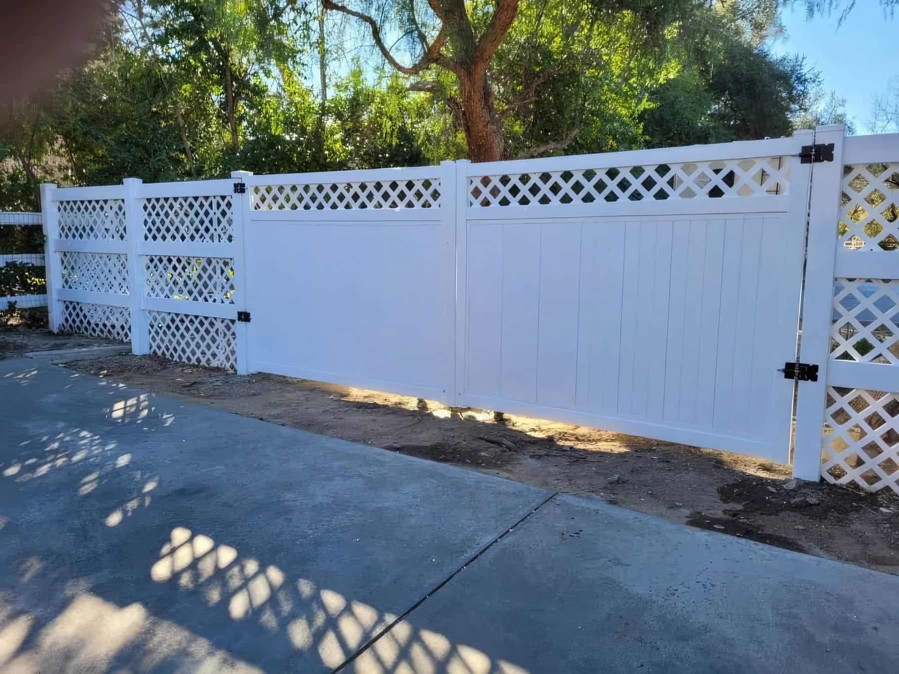 Vinyl driveway double gates with lattice fence beside leading into the suburban home with trees in the background