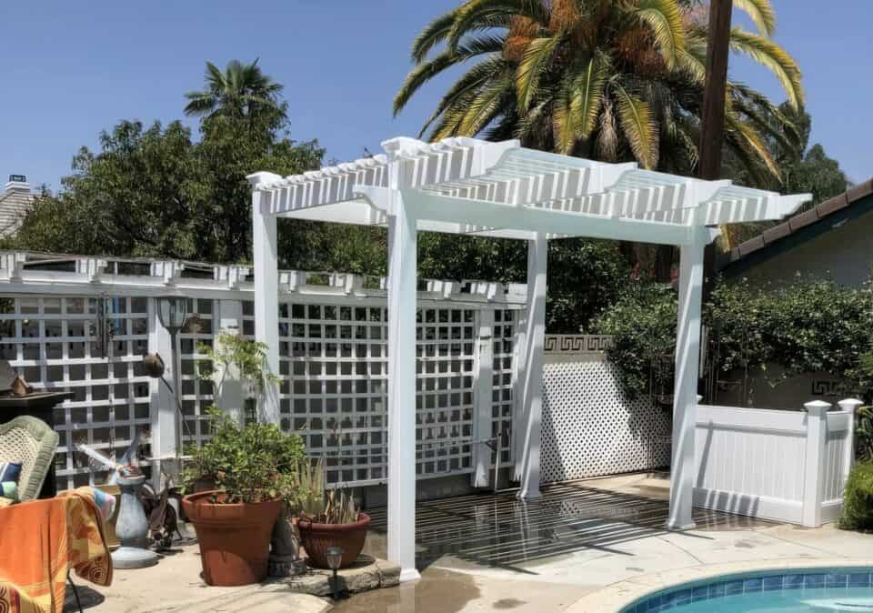 Vinyl free standing patio cover with potted plants & poolside, surrounded by trees & concrete sidewalk - a serene outdoor oasis.