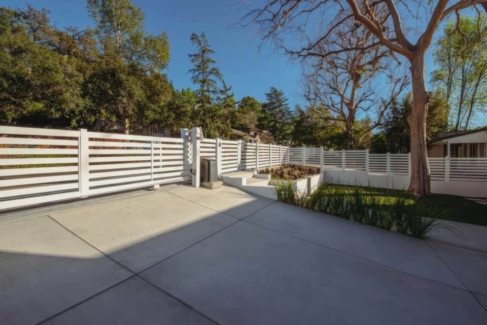 Vinyl horizontal picket fence, concrete driveway, lush lawn, trees in the background - a serene suburban landscape.