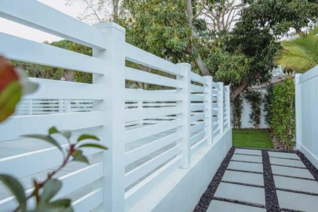 Vinyl horizontal picket fence, concrete sidewalk & driveway, front lawn, trees in background: A charming suburban scene.