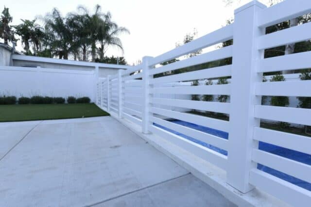 "Vinyl horizontal picket fence, concrete floor, small garden, lush lawn & trees in background - a charming outdoor oasis.