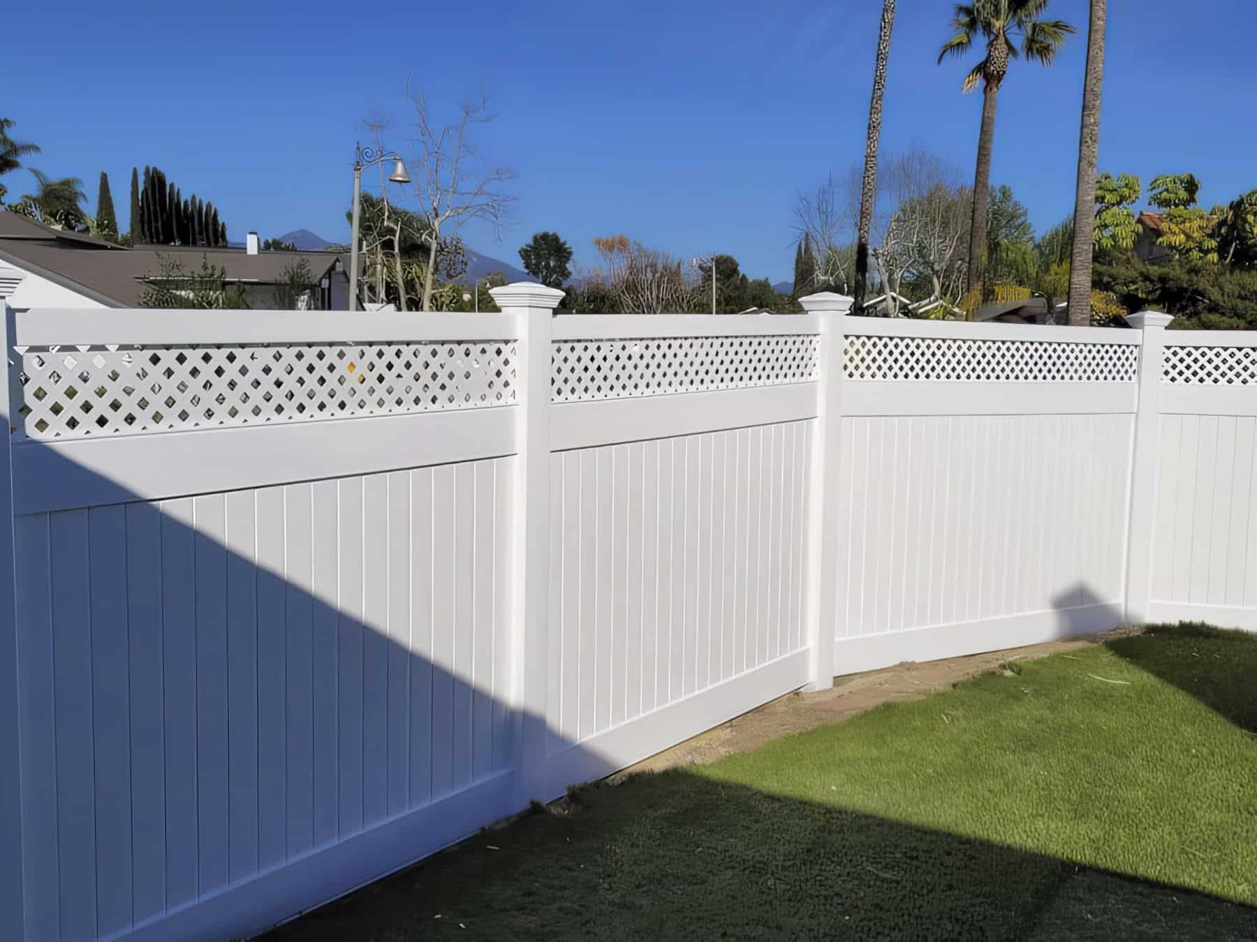 Vinyl horizontal picket fence surrounding small garden, concrete floor, lush grassy lawn, with trees in the background.