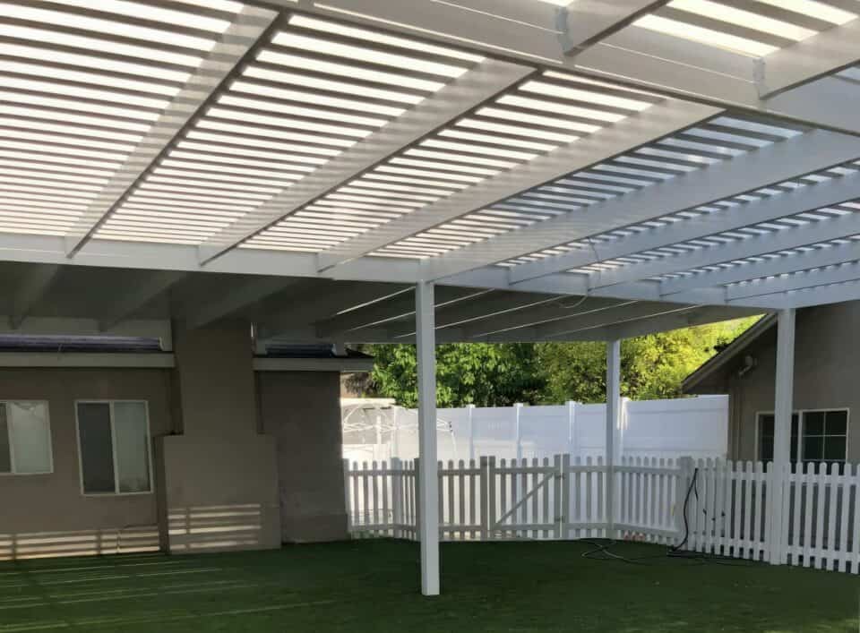 Poolside vinyl louvered patio cover above relaxing outdoor chairs and tables with trees in the background