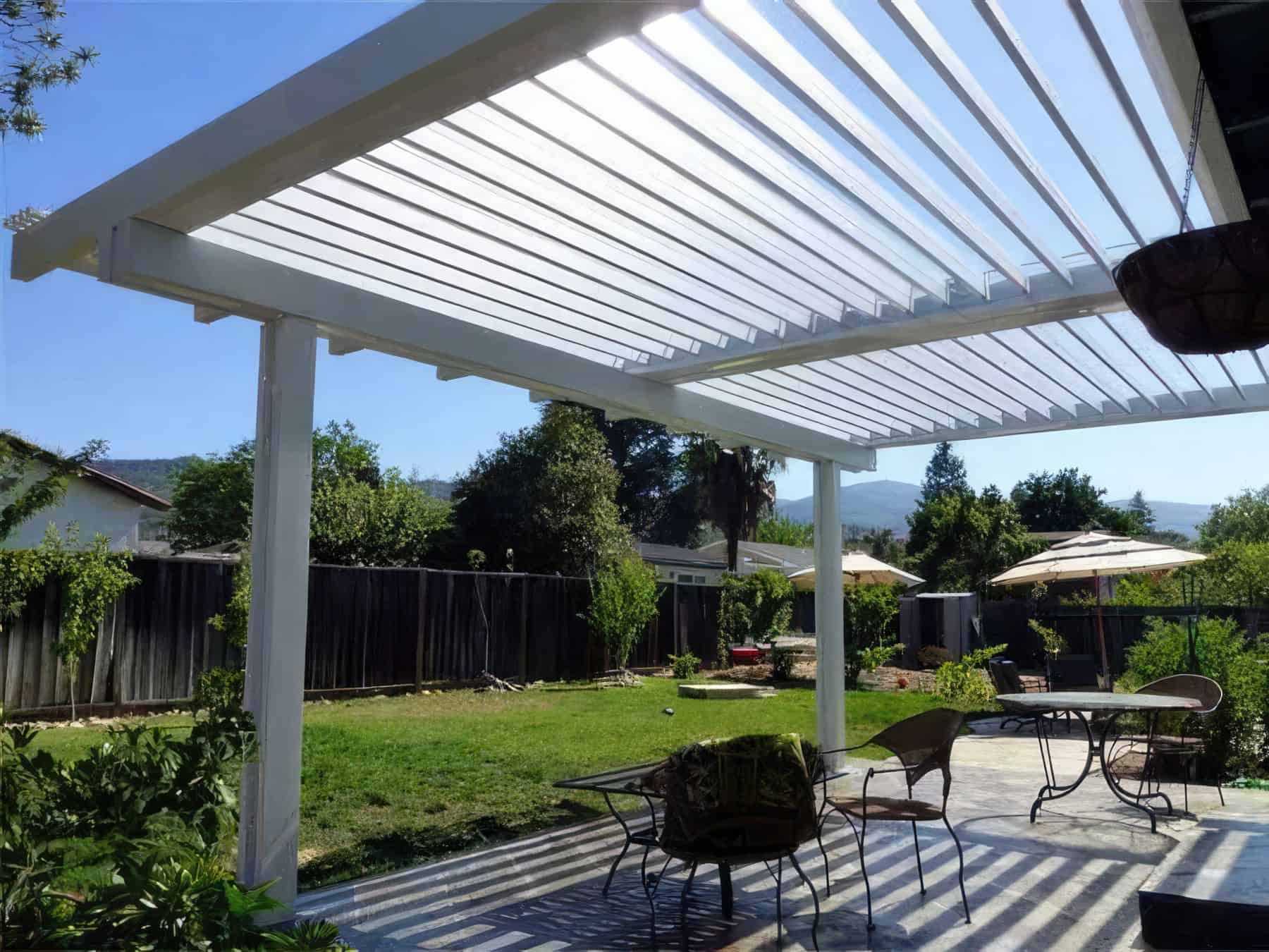Vinyl louvered patio cover above backyard retreat with potted plants and large trees in the background