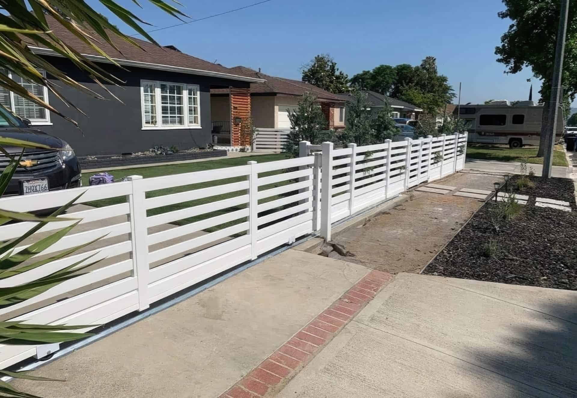 Vinyl picket fence behind large tree on front lawn with marble steps and hedge wall with a tall hedge wall.