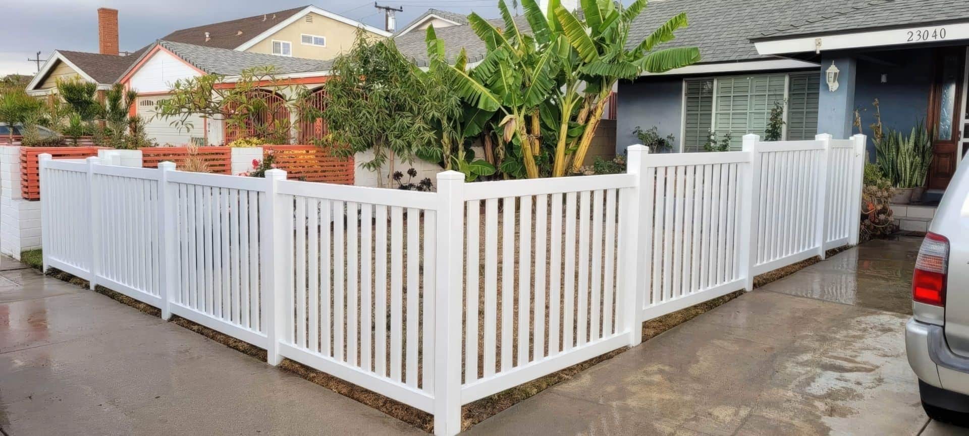 Vinyl picket fence connected to metal chain fence separate the backyard hedge and garden from the concrete sidewalk