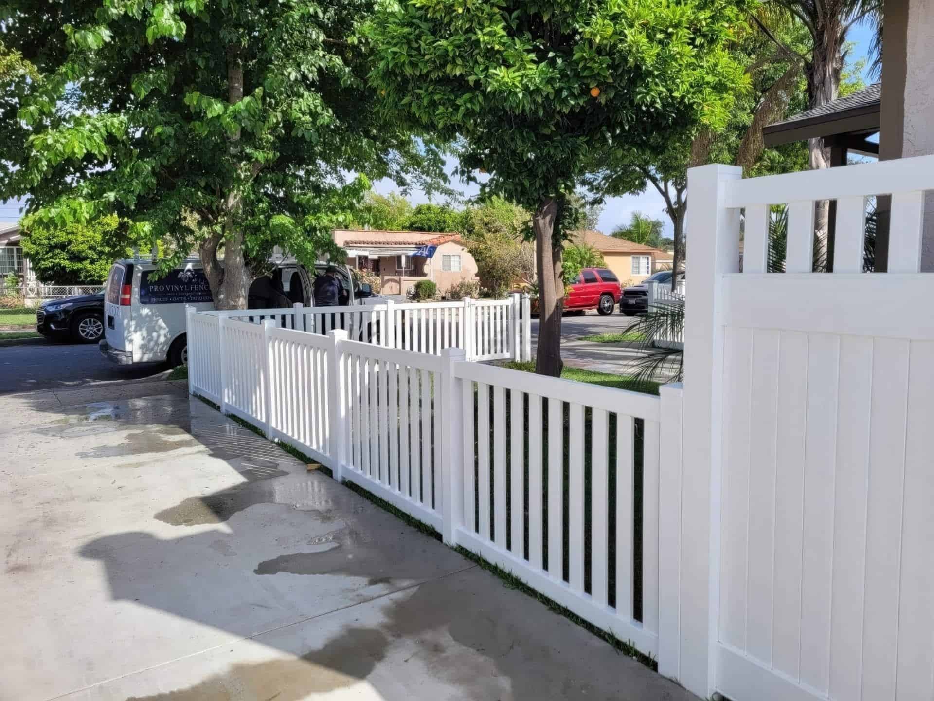 Vinyl picket fence with gate leading into side entrance of home under wooden shade