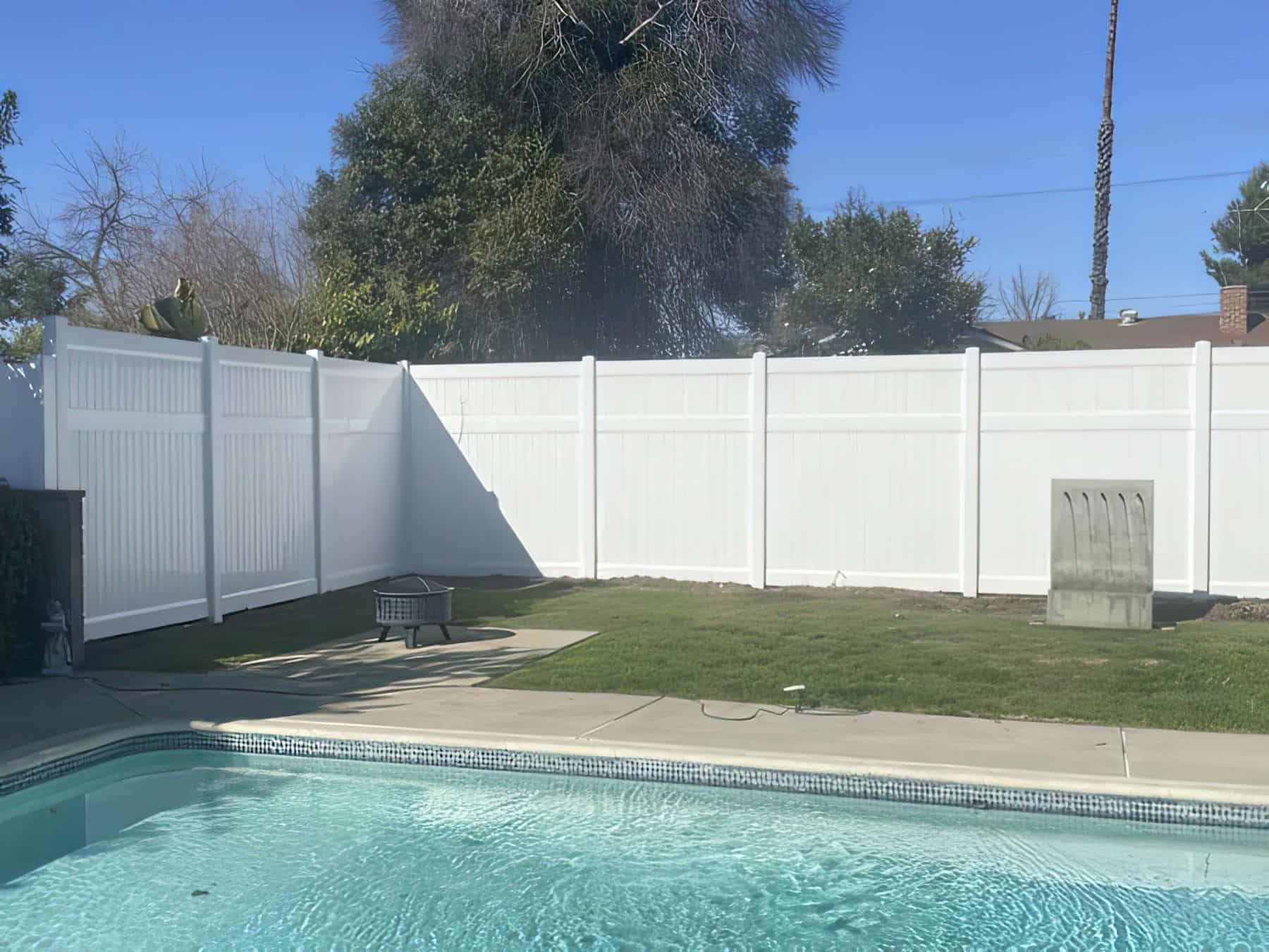 Vinyl pool fence from patio entrance leads into cliff-face tropical themed pool palm trees and other garden patches