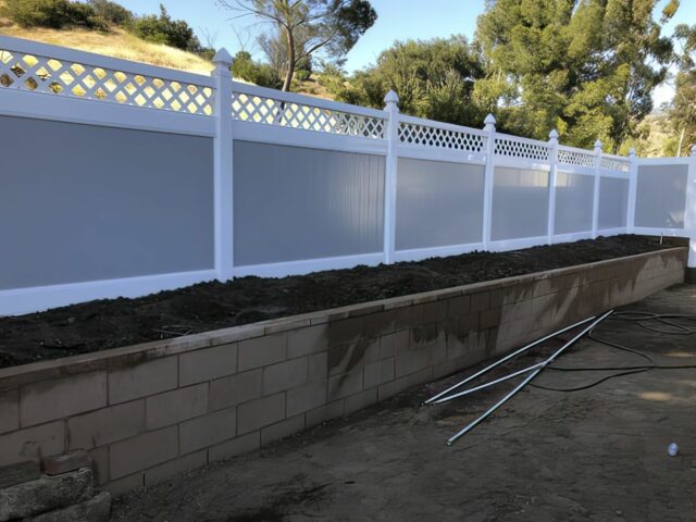 Vinyl privacy and lattice fence separating the grassy front lawn from the sidewalk and other houses in distance with trees