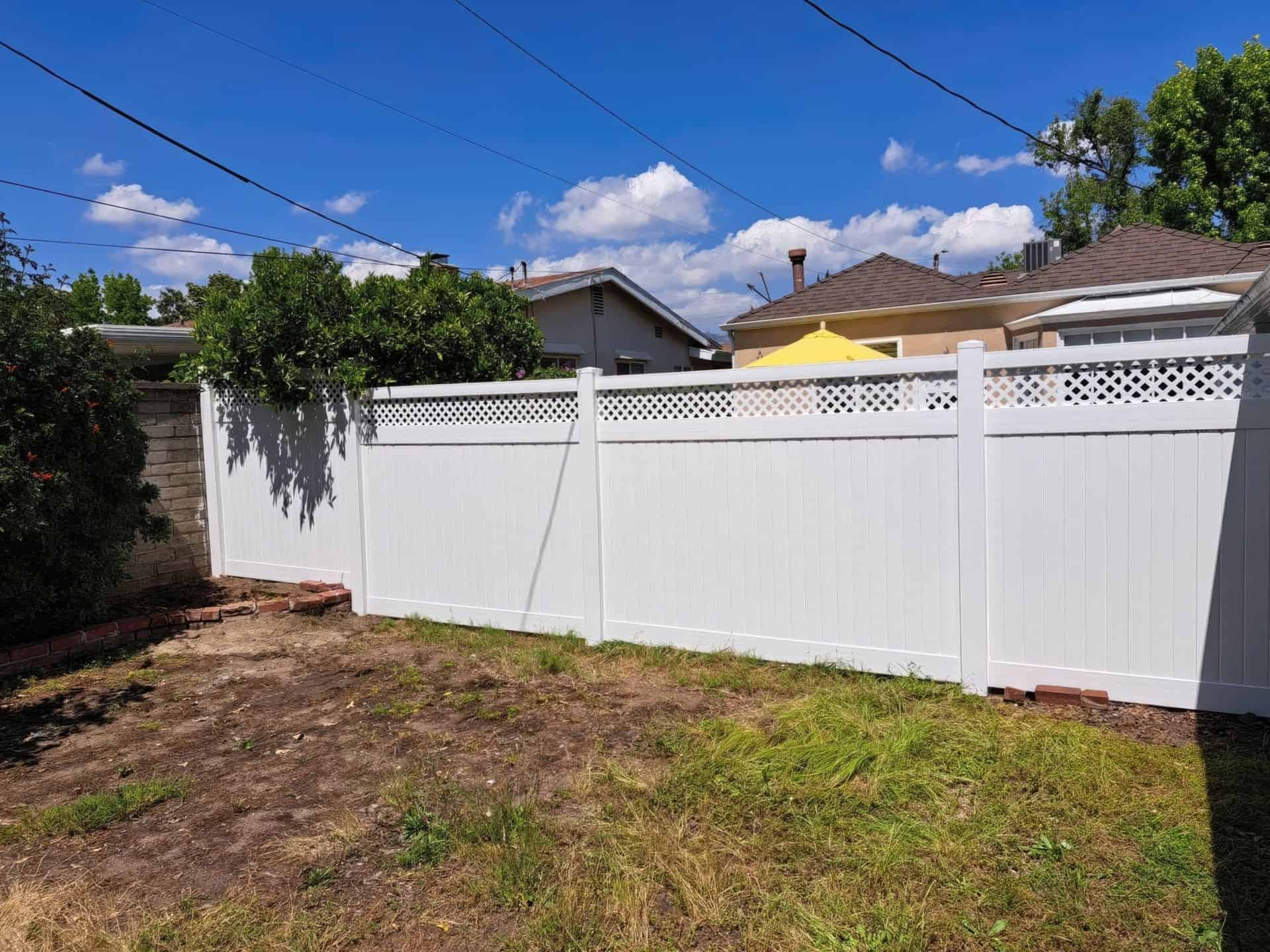 Vinyl privacy and lattice fence connected to gate leading into concrete walkway beside grassy front lawn leading into porch.