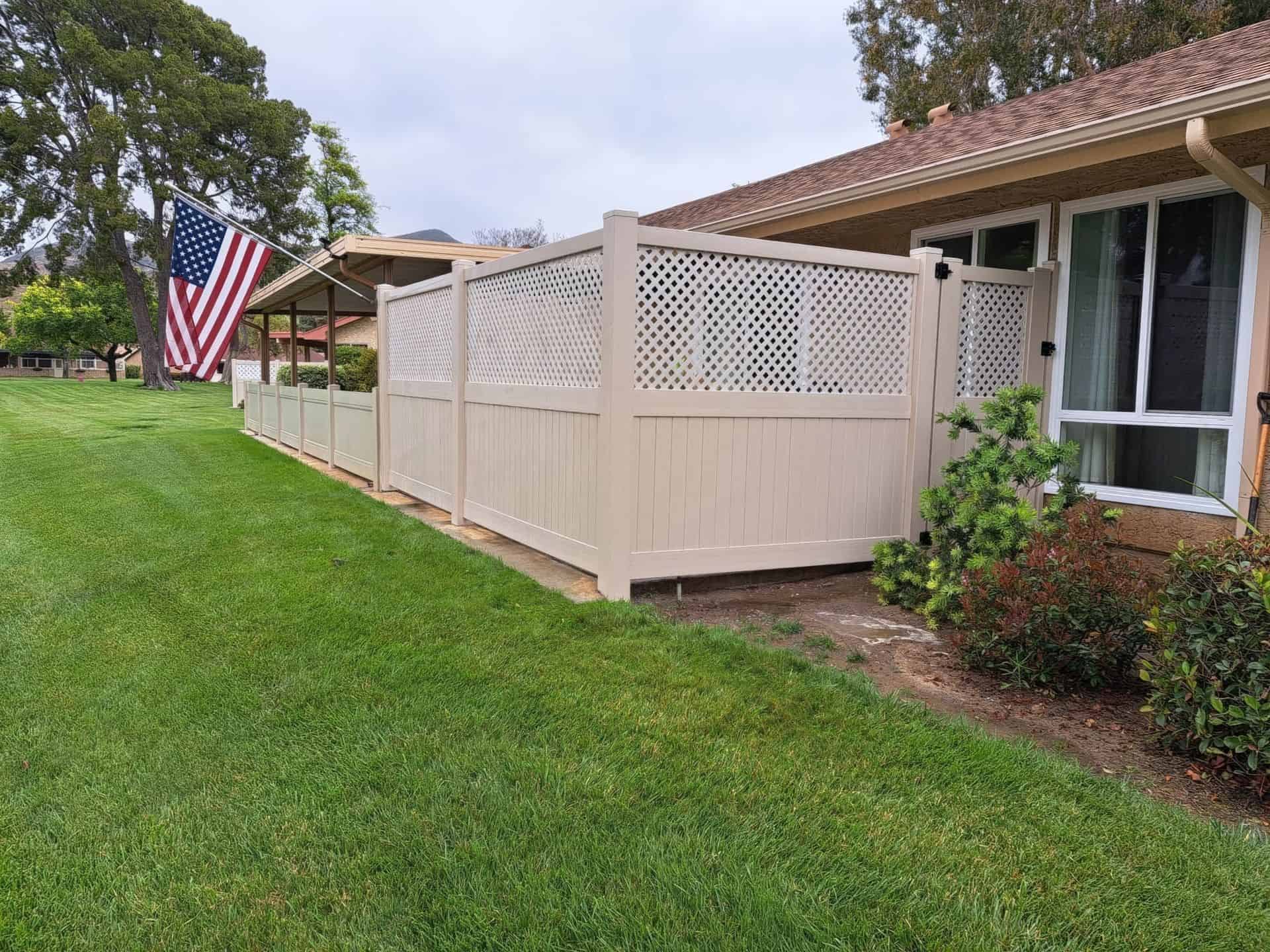 Vinyl privacy and lattice fence beside small shrubs and bushes around surrounding grass and patio shade