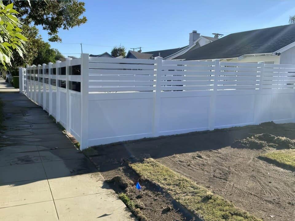 Vinyl privacy and picket fence connected to fence with reflective glass separating the inside lawn and sidewalk.