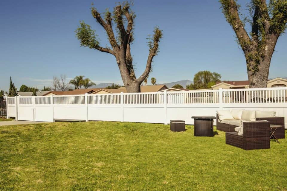 Vinyl privacy and picket fence behind an open backyard with comfortable seating area and in front of giant trimmed tree